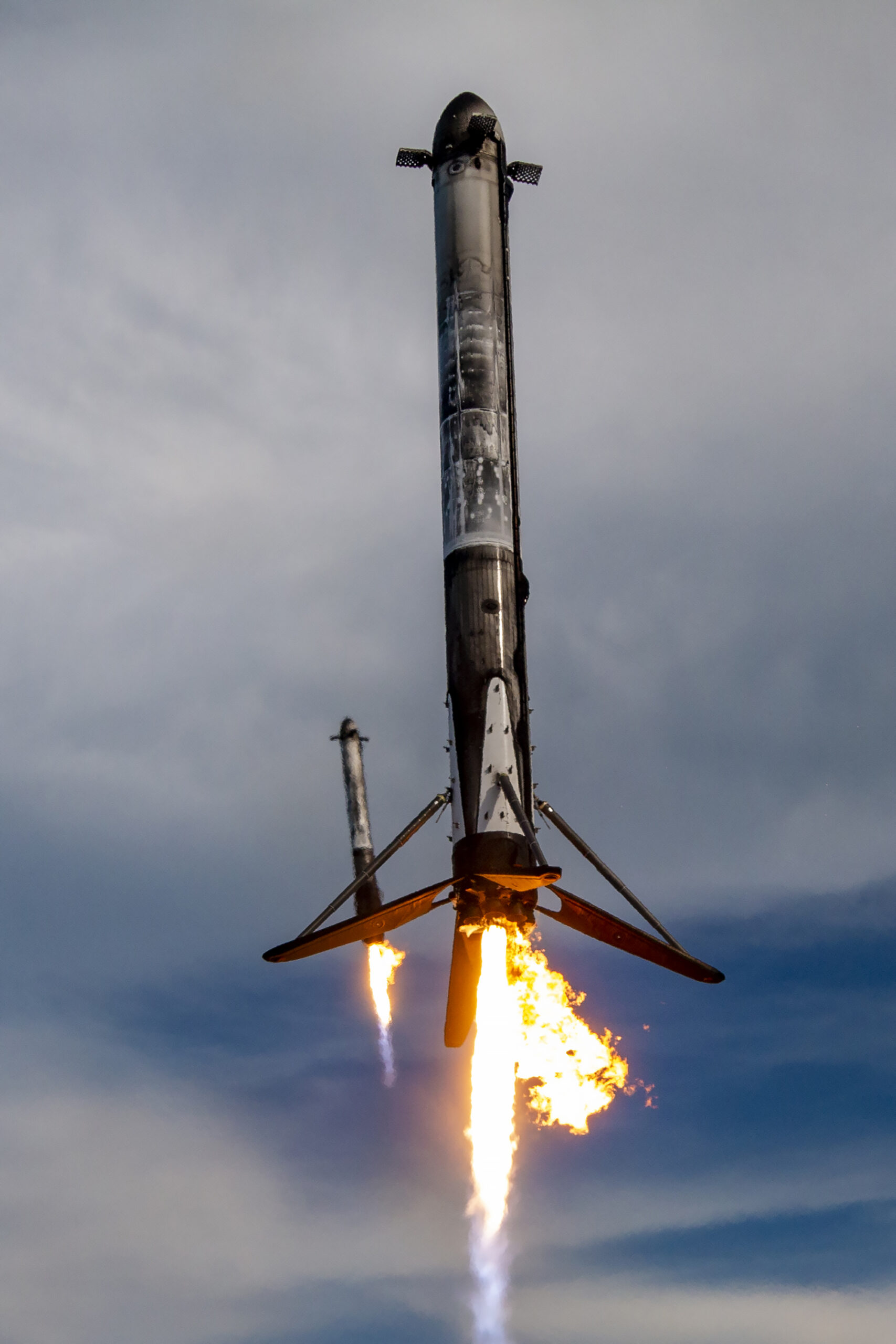Dois boosters do Falcon Heavy descendo com chamas para pouso sincronizado